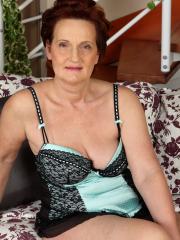 Redheaded granny with augmented boobs takes off her brassiere to get naked